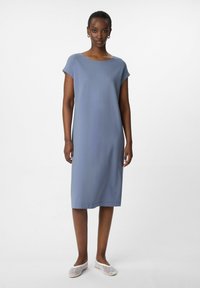 Blaues Baumwollkleid mit kurzen Ärmeln, Rundhalsausschnitt und geradem Schnitt, der bis zur Mitte der Wade reicht; kombiniert mit weißen Netzschuhen.