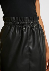 Svart läderkjol med elastisk midja, dubbla dragskor och metallaccenter, med en mjuk yta och elegant design.