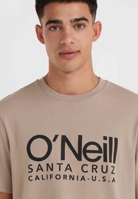 Béžové bavlněné tričko s velkým černým textem "O'Neill SANTA CRUZ CALIFORNIA-U.S.A." na přední straně; kulatý výstřih, krátké rukávy.