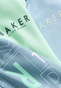 Gaisza zaļgana un zila kokvilnas auduma, kurā redzams teksts "BAKER" tumšā un baltā krāsā. Mīksta tekstūra, slāņota konstrukcija ar izteiksmīgiem burtiem un akcentiem.