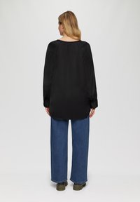 Zwarte lange-sleeve shirt met een losse pasvorm, ronde halslijn en knoop cuffs, gecombineerd met brede blauwe spijkerbroeken en groene laarzen.