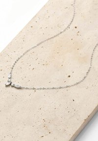 Silberne Halskette mit feiner Kette und drei dekorativen Akzenten, die eine glatte Textur und minimalistisches Design aufweist, auf einer hellen Steinoberfläche ruhend.