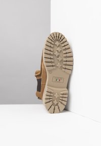 Botte en daim tan avec une semelle en caoutchouc beige dotée d'un motif de crampons rugueux et d'un accent textile marron. L'étiquette indique "Nero Giardini, Fabriqué en Italie."