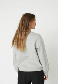 Felpa grigia con scollo rotondo, maniche lunghe e polsini a costine. Tessuto morbido e spazzolato, vestibilità rilassata e design in un unico colore.