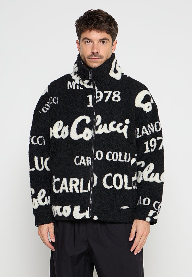 Schwarze Fleecejacke mit hohem Kragen, durchgehendem Reißverschluss und kontrastierenden weißen Textmustern. Weiche Textur mit lässigem Schnitt.