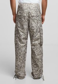 Cargo bukser i camouflagemønster, med en afslappet pasform, flere lommer, elastiske nederste kanter og et afdæmpet beige- og gråfarvet skema.