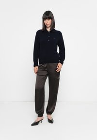 Maglione azzurro in maglia con colletto e bottoni, abbinato a pantaloni jogger marroni lucidi. I pantaloni hanno polsini elasticizzati e un dettaglio con zip laterale.
