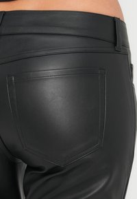 Μαύρο δερμάτινο παντελόνι με λεία υφή, που διαθέτει πίσω τσέπη με ραμμένη ραφή. Η μέση είναι κομψή και εφαρμοστή.