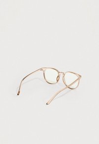 Διαφανή μπεζ πλαστικά πλαίσια γυαλιών με στρογγυλεμένους τετράγωνους φακούς, ανοιγμένα και τοποθετημένα σε απλή λευκή επιφάνεια.