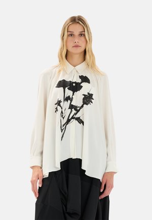 Camicia bianca con bottoni e maniche lunghe, caratterizzata da una stampa floreale nera sul davanti. Il tessuto è leggero e fluido.