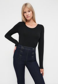 Haut noir à manches longues avec un décolleté arrondi, associé à un jean en denim foncé taille haute, comportant six boutons sur le devant et une coupe ajustée.