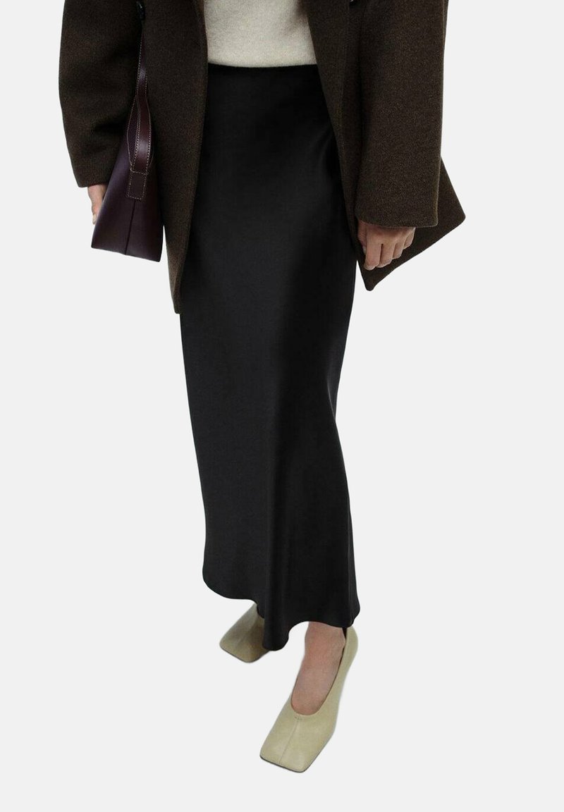 Schwarze Satinstreifenmaxihose kombiniert mit beigen flachen Schuhen mit quadrater Zehenform. Das Outfit wird durch einen braunen Mantel und eine kleine burgunderfarbene Handtasche ergänzt.