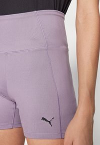Fioletowe, wysokiej talii szorty sportowe wykonane z elastycznego materiału, z czarnym logo Pumy na dolnej stronie i widocznymi detalami szwów.
