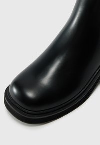 Bota de cuero negro con punta redondeada, acabado suave y una ligera suela elevada. Presenta una suela exterior de goma resistente con un borde texturizado.