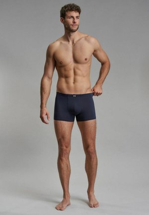 Dunkelblaue Boxer-Shorts aus dehnungsfähigem Material, mit einer glatten Textur und einem elastischen, markenbeschrifteten Bund, auf einem männlichen Modell präsentiert.