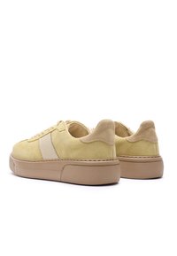 Żółte zamszowe trampki z kremowym paskiem, okrągłym noskiem, grubą beżową podeszwą i teksturowanymi akcentami. W zestawie sznurowadła i pętelka na pięcie.