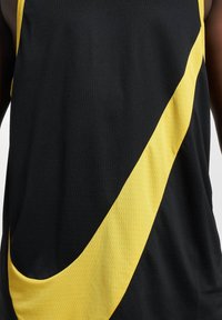 Svart atletisk tank topp laget av teksturert stoff med et fremtredende gult diagonalt stripe over fronten.