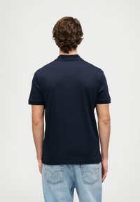 Námorně modré polo tričko s krátkým rukávem, vyrobené z hladké tkaniny. Má klasický límeček a detail ve tvaru V na zadní straně.