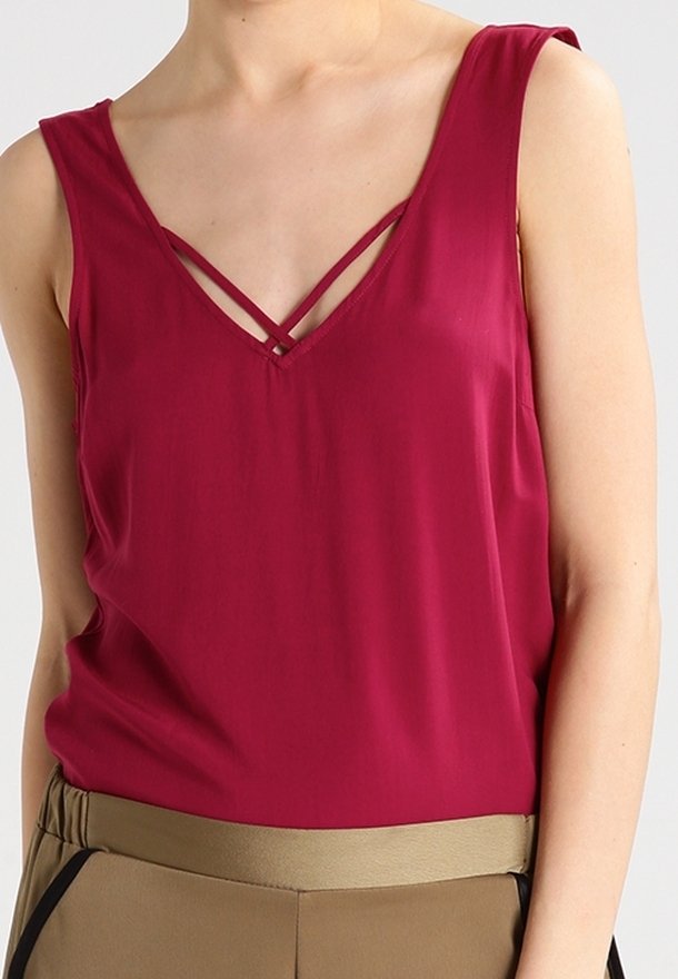 Top sans manches bordeaux, avec un décolleté en V et des bretelles croisées, fabriqué dans un tissu lisse et léger. Assorti à un pantalon beige à taille haute.