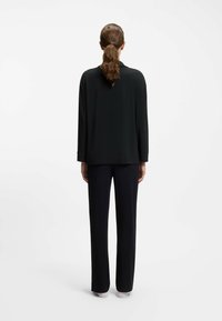 Black long-sleeve shirt with a straight cut and turned-up cuffs, paired with straight-leg black trousers, viewed from the back.
