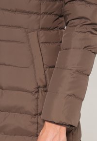 Brązowa kurtka puchowa z haftowanymi ukośnymi panelami, boczną kieszenią oraz gładką, błyszczącą teksturą. Rękaw ma dopasowane wykończenie.