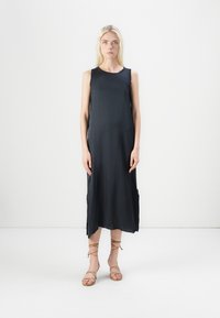 Rochie neagră fără mâneci, până la genunchi, dintr-un material neted, cu o croială ușor lejeră, cu fante laterale, purtată cu sandale cu toc subțire de culoare bej, design minimalist, fundal simplu.