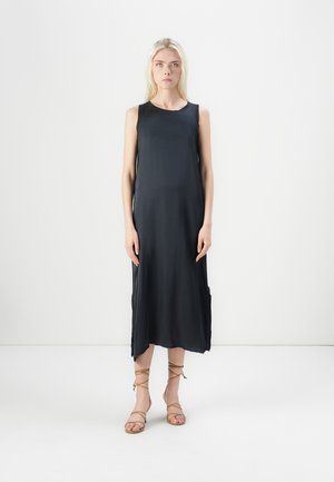 Black sleeveless dress, knee-length, smooth fabric, slightly loose fit, side slits, worn with tan strappy sandals, minimal design, plain background.