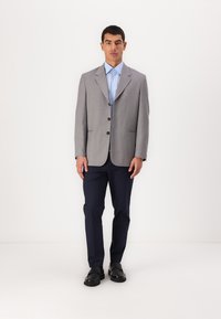 Grå stripete blazer med hakkede slag, tre knapper og to frontlommer, sammen med en lyseblå skjorte og mørkeblå bukser.