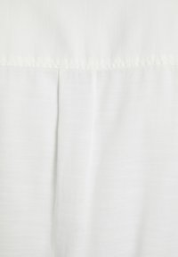 Tessuto bianco con una superficie texture, caratterizzato da un sottile motivo orizzontale e cuciture visibili lungo il bordo superiore. Aspetto complessivo liscio.