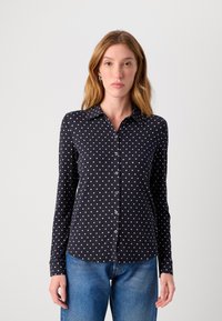 Marineblå langermet skjorte med hvite prikker, knappestolpe-design, spiss krage, laget av mykt stoff. Brukt sammen med blå jeans.