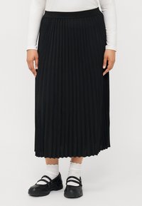 Svart plisserad kjol med bred midjeband, som når till mitt på vaden. Dressed med en långärmad vit topp och svarta skor med remmar.