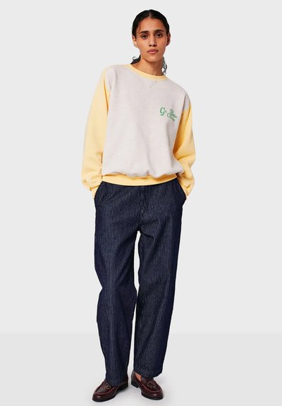 Sweatshirt in light gray with yellow sleeves, featuring green embroidered text. Paired with navy pinstriped pants and dark shoes.