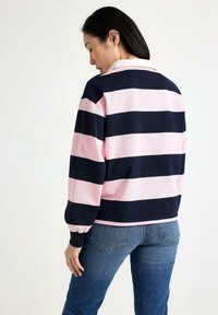 Langærmet polo t-shirt med skiftende marineblå og lys pink striber; har en hvid krave og ribbede manchetter, parret med blå jeans.