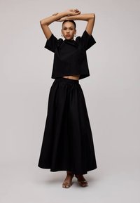 Fekete, rövid ujjú, kerek nyakú, cropped top, fekete, magas derekú, hosszú szoknyával párosítva. Sima anyag és egyszerű dizájn.