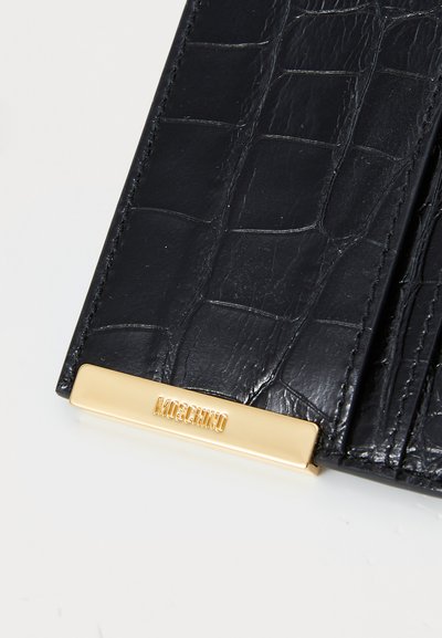 Portofel negru din piele cu textură de crocodil, având un plăcuță logo Moschino de culoare aurie. Formă rectangulară cu detalii de cusătură vizibile.