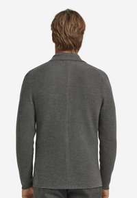 Graue gestrickte Strickjacke, gerippte Textur, lange Ärmel, Reverskragen, mittellanger Rücken und gerader Schnitt mit einer Mittelnaht.