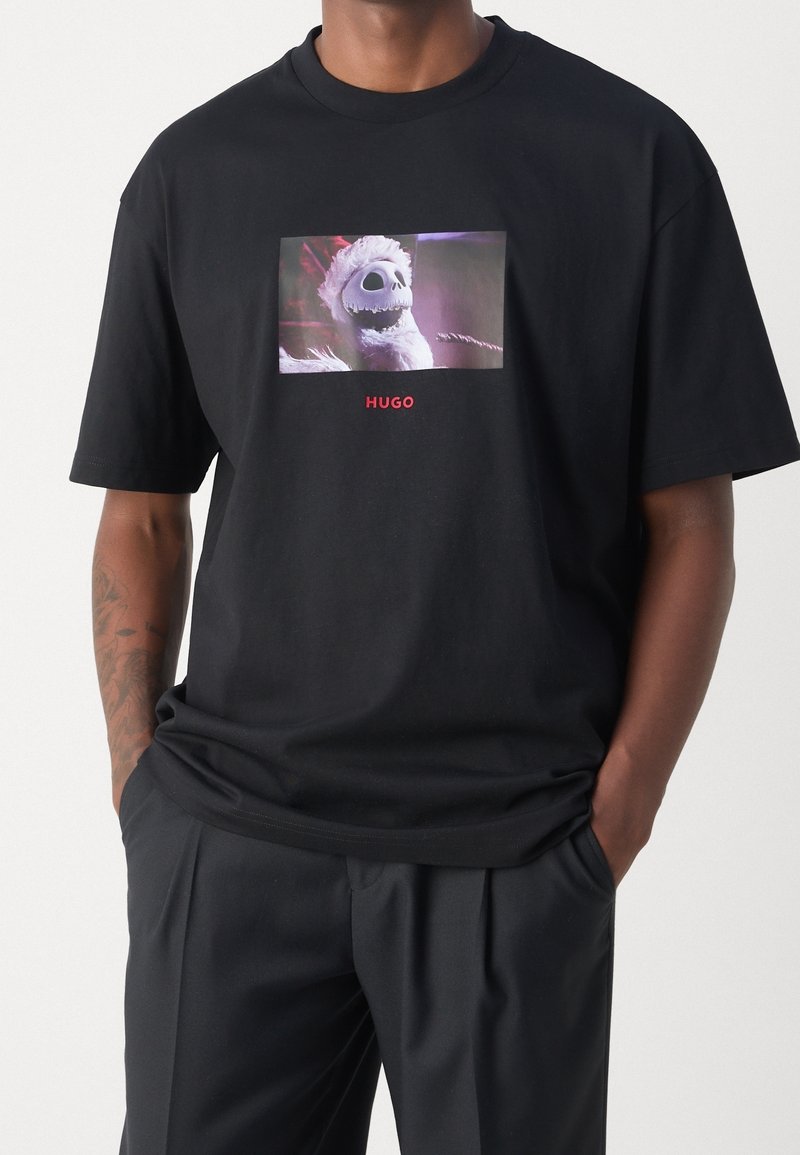 Schwarzes Baumwoll-T-Shirt mit einem grafischen Druck eines Charakters, darunter in rotem Text "HUGO". Kurze Ärmel und Rundhalsausschnitt.