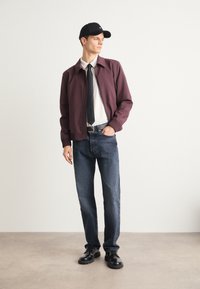 Burgundi värvi suleline jakk valge särke, must lips, tumedad teksased ja mustad saapad, mille peale on pandud must müts. Lihtne, modernne disain.