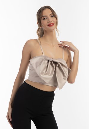 Lys beige crop top i satin med en stor sløjfe detalje foran, tynde stropper og en tætsiddende silhuet. Sammen med sorte leggings.