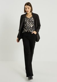 Blazer noir sur un haut à motifs imprimé animalier en beige et noir, associé à un pantalon noir et des bottines noires à la cheville.
