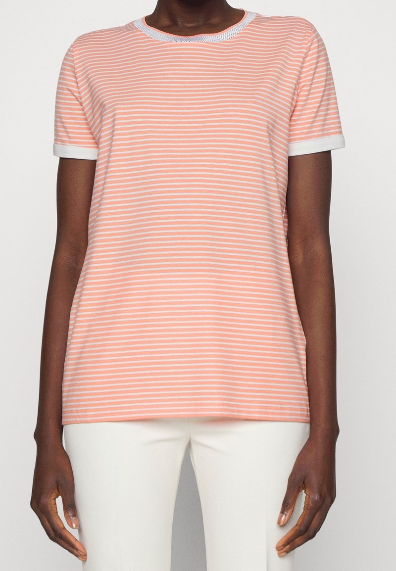 Personne portant un T-shirt à manches courtes rayé rose pâle et blanc avec des bordures blanches, accompagné d'un pantalon blanc.