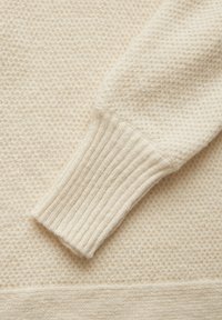 Cremfarbener Pullover mit strukturiertem Strickmuster und gerippten Bündchen. Weicher Stoff mit glatter Oberfläche, der ein minimalistisches Design zur Schau stellt.