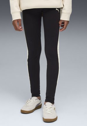 Leggings noirs avec des bandes latérales crème, dotées de fermetures à pression. Associés à des baskets crème avec des semelles brunes et des accents gris.