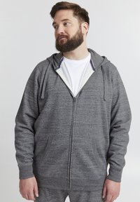 Sudadera con cremallera gris de tela texturizada, con dos bolsillos frontales y capucha ajustable con cordón. Presenta un forro blanco cerca de la cremallera.