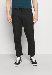 Zwarte joggers met elastische taille en een trekkoord, taps toelopende pasvorm en zijzakken, gecombineerd met zwart-witte sneakers.