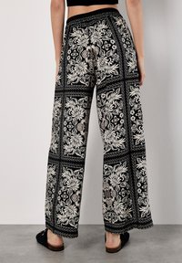Schwarz-weiße, blumengemusterte weit geschnittene Hose mit elastischem Bund, die eine Mischung aus aufwendigen Textildesigns und einem lockeren Schnitt bietet.