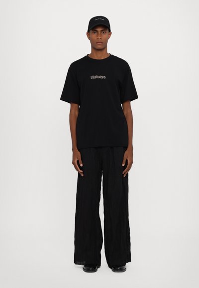 Camiseta gráfica negra con el texto "LES BENJAMINS", combinada con pantalones holgados negros y una gorra a juego, que presenta un visera plana y un diseño minimalista.