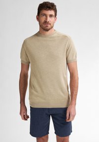 Beige gestrickter Kurzarmpullover mit Rundhalsausschnitt und gerippten Bündchen, kombiniert mit navy-blauen gestreiften Shorts. Glatte Textur, einheitliche Farbe, lässige Passform.