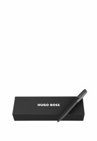 Čierne guľôčkové pero s textúrovaným úchopom položené na čiernej obdĺžnikovej škatuľke s bielym logom "HUGO BOSS".