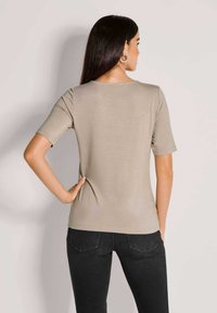 Beige T-Shirt mit kurzen Ärmeln aus weichem Stoff, mit Rundhalsausschnitt und taillierter Silhouette. Getragen mit dunklen Jeans.